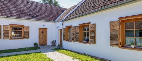 A traditional building with a tiled roof, wooden shutters, and a paved courtyard.