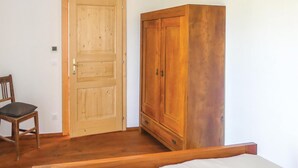 A room with a wooden door, a wooden wardrobe, a wooden chair, and a bed.