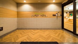 En hotellobby med ett trägolv i fiskbensmönster, en receptionsdisk och en skylt med texten ”Välkommen till SUPER HOTEL”.