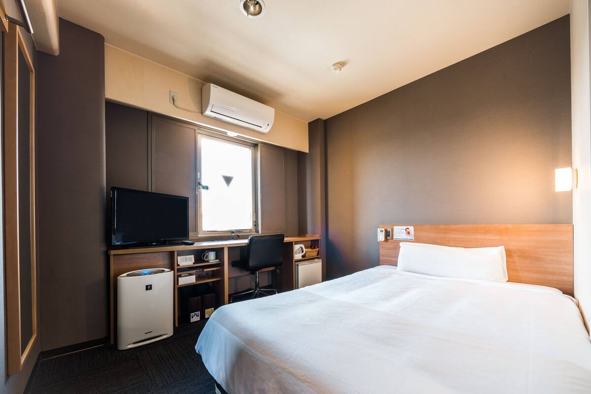 Habitación de hotel con una cama grande, un escritorio con computadora, televisor y una kitchenette pequeña.