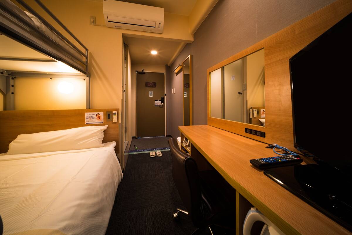 Una habitación de hotel con cama, escritorio con espejo, televisión y aire acondicionado.