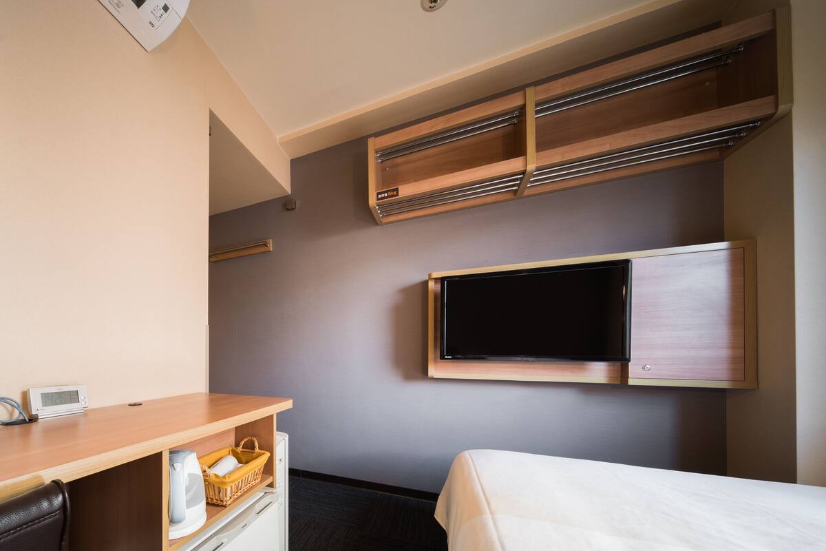 Una habitación de hotel con cama, escritorio con tetera, televisión y estante empotrado.