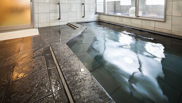 En modern inomhuspool med väggar av genomskinligt glas, ett kaklat golv och ett metallräcke.