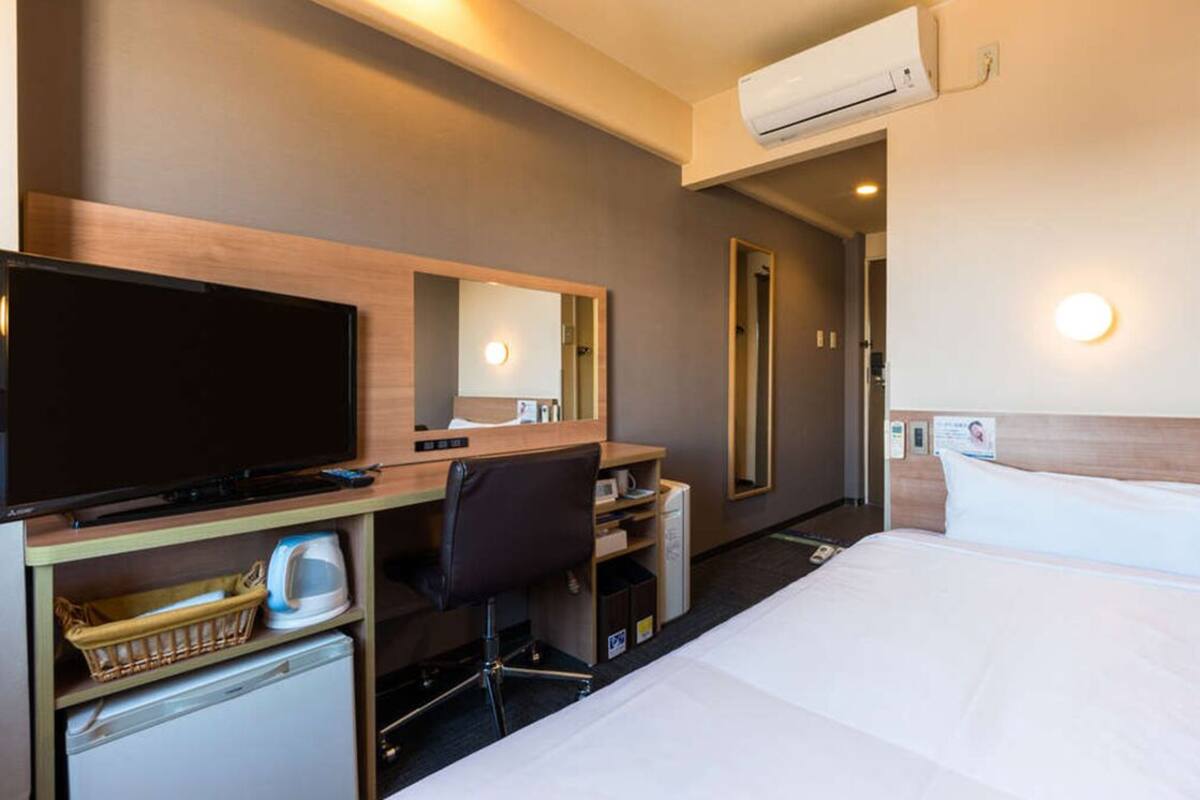Habitación de hotel con cama, escritorio, silla, televisor, microondas y refrigerador pequeño.