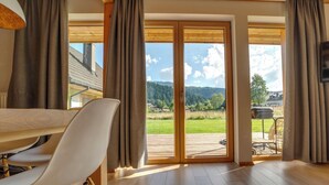 A spacious room with a wooden floor, a dining table with chairs, large sliding glass doors leading to a deck, and a view of a green landscape. - Chaty Pod Beskidkiem by Interhome (Szczyrk)