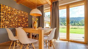 A dining area with a wooden table and chairs, a vase with flowers, and a wall of stacked logs. - Chaty Pod Beskidkiem by Interhome (Szczyrk)