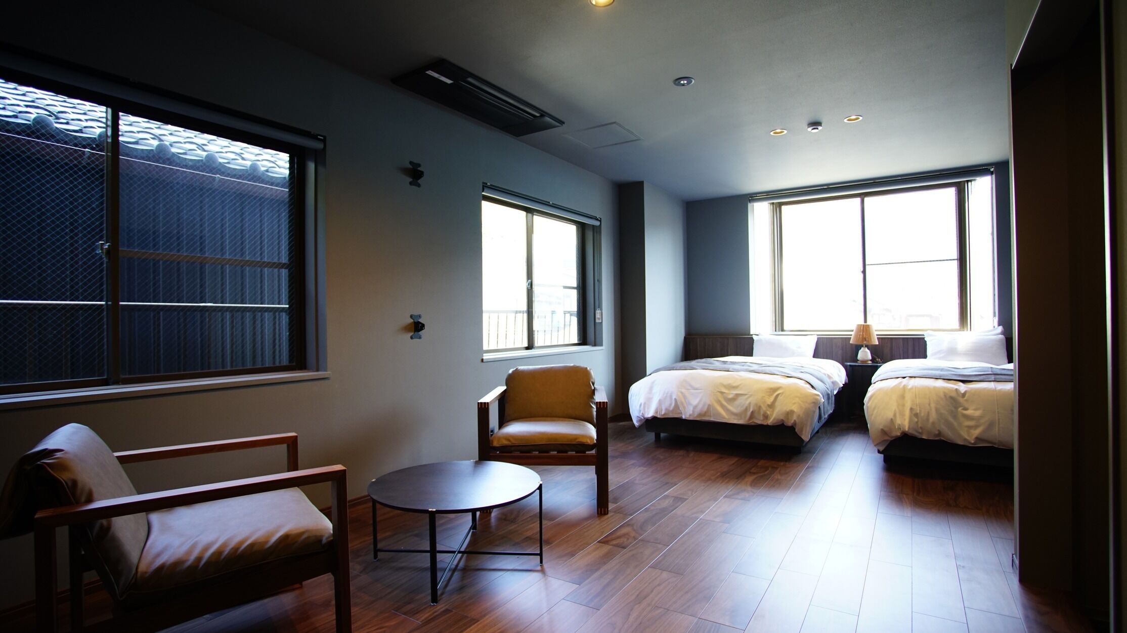 Ein Hotelzimmer mit zwei Betten, einem kleinen Tisch, einem Stuhl und großen Fenstern.