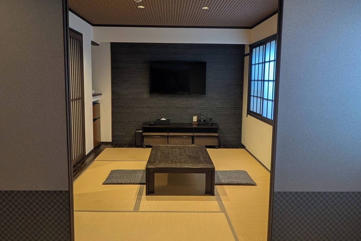 Una tradizionale stanza giapponese con pavimento in tatami, un tavolino, una TV montata a parete e porte scorrevoli.