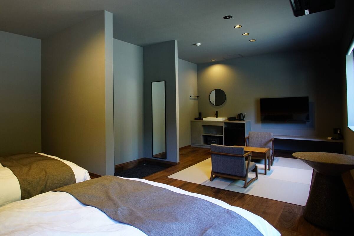 Una moderna camera d'albergo con un letto, una scrivania, una sedia, un tavolino, uno specchio, una TV e un lavandino.