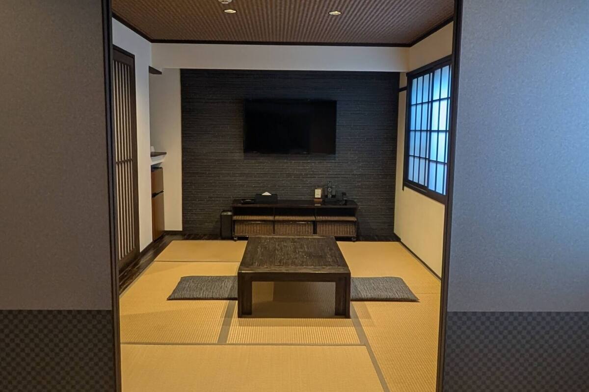 Una tradizionale stanza giapponese con pavimento in tatami, un tavolino, un televisore montato a parete e porte scorrevoli.