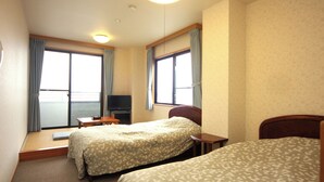 Quarto de hotel com duas camas, televisão e janela com cortinas.