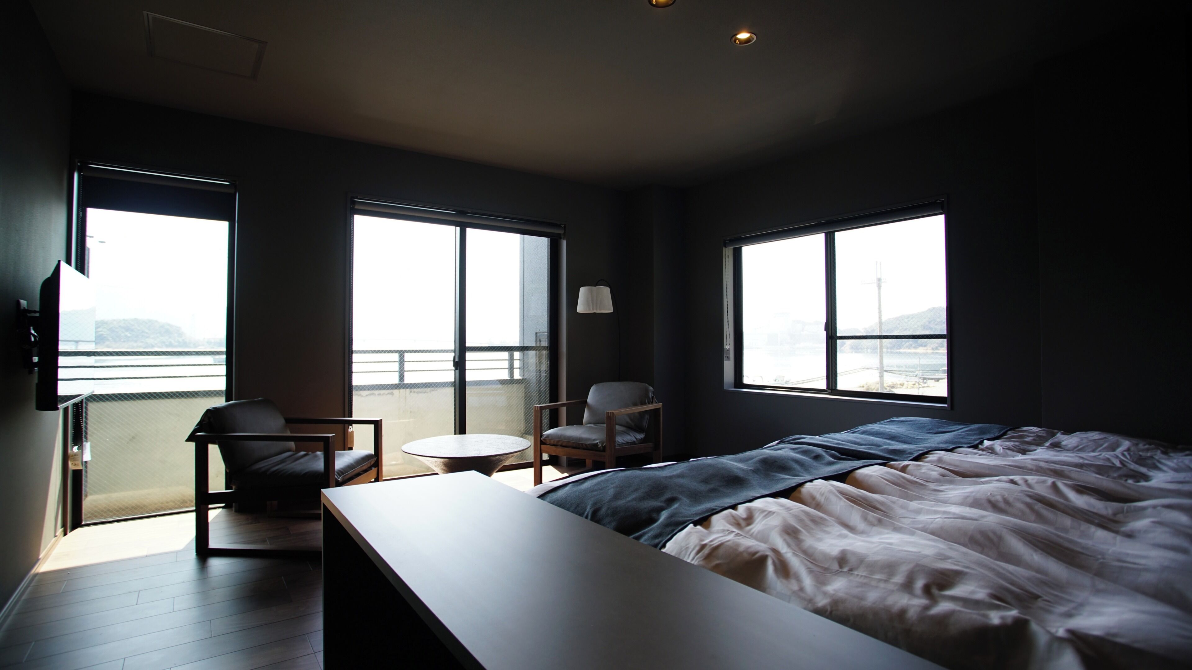 Ein Schlafzimmer mit einem Bett, einem Sessel, einem kleinen Tisch und großen Fenstern.