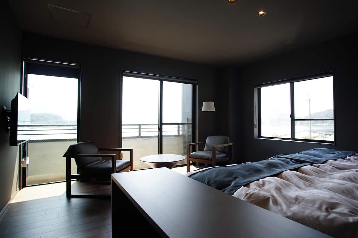 Ein Schlafzimmer mit einem Bett, einem Sessel, einem kleinen Tisch und großen Fenstern.