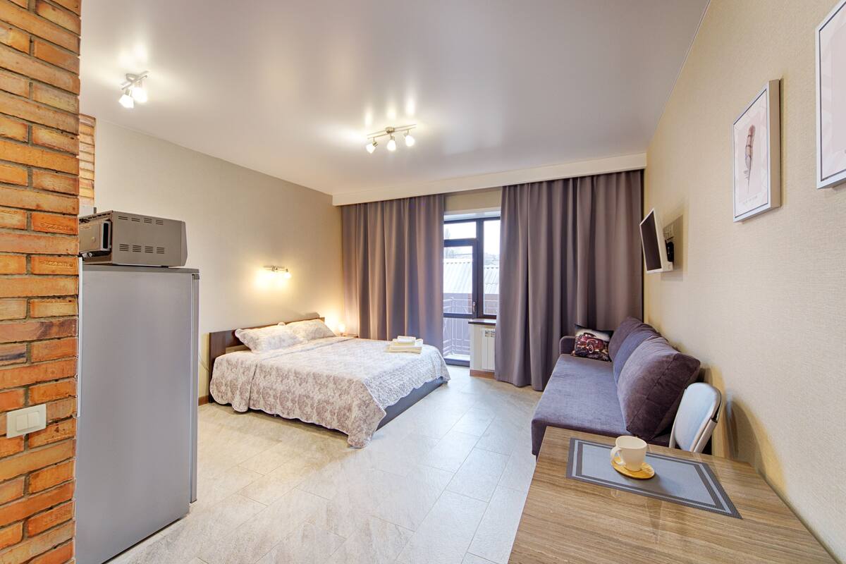 A hotel room with a bed, a sofa, a small table with a cup, a TV, and a window with curtains.