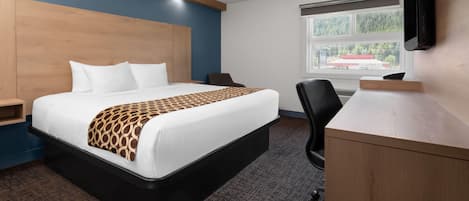 Quarto de hotel com cama, escrivaninha, cadeira e janela com vista para um edifício.
