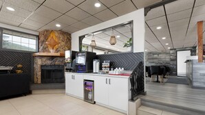 A modern hotel lobby with a stone accent wall, a fireplace, a self-service kiosk, and a seating area with a view of the outdoors. - Travelodge by Wyndham Blairmore (Blairmore)