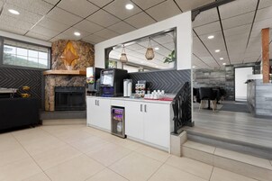 Un vestíbulo de hotel moderno con una pared de acento de piedra, una chimenea, un quiosco de autoservicio y una zona de estar con vistas al exterior.