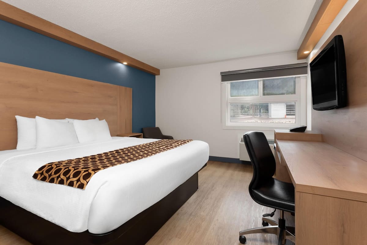 A hotel room with a large bed, a desk, a chair, a TV, and a window with a view.
