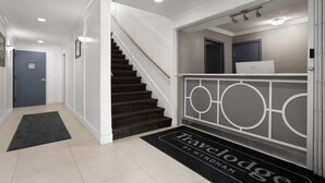 A clean, modern hallway with a staircase leading to a landing. A laptop is visible on a counter, and a doormat with the name "Travelodge by Wyndham" is placed at the entrance. - Travelodge by Wyndham Blairmore (Blairmore)