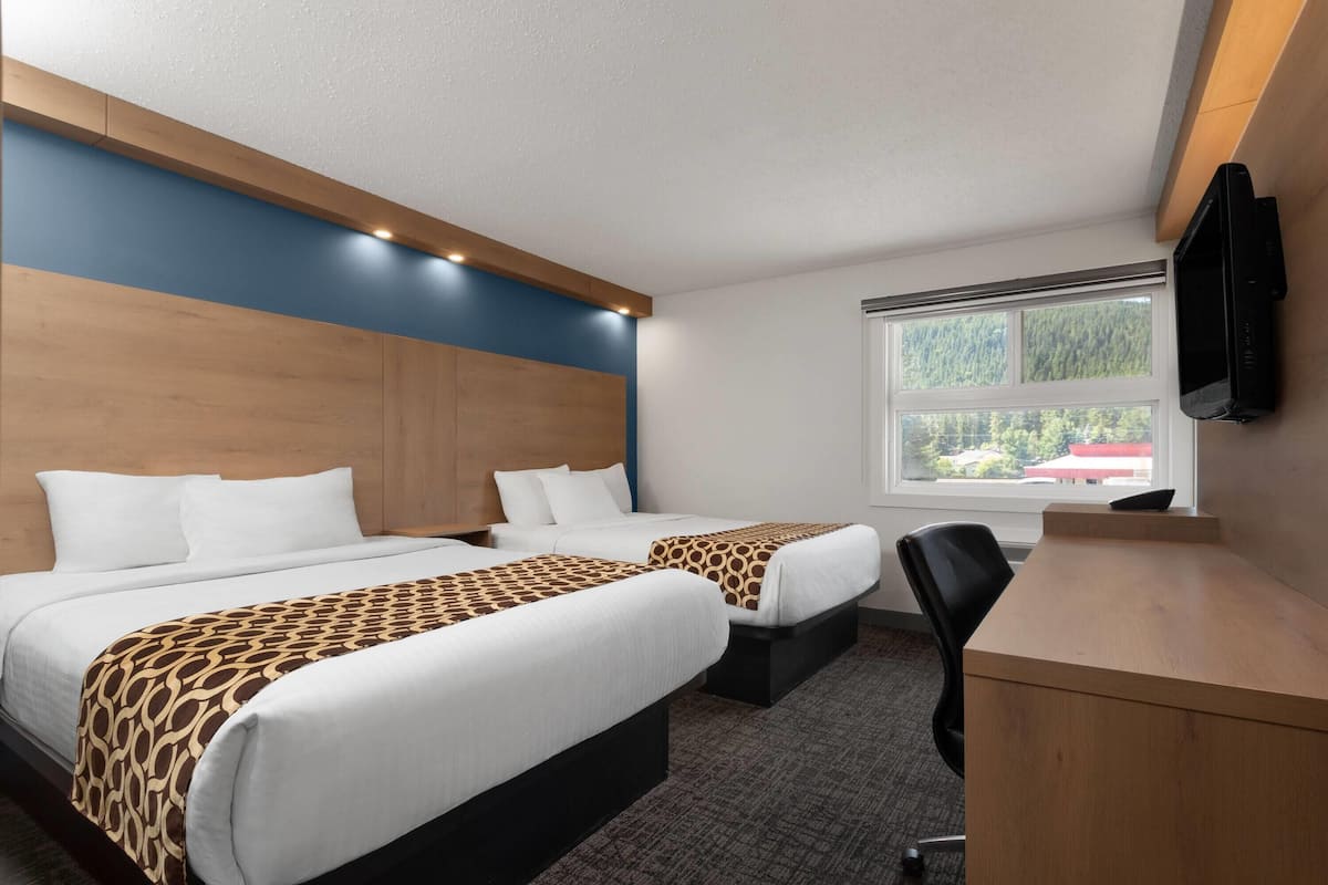 A hotel room with two beds, a desk, and a TV.