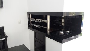A modern kitchen with black countertops, stainless steel appliances, and a built-in wine rack. - Casa da Piscina Bento Gonçalves (Bento Gonçalves)