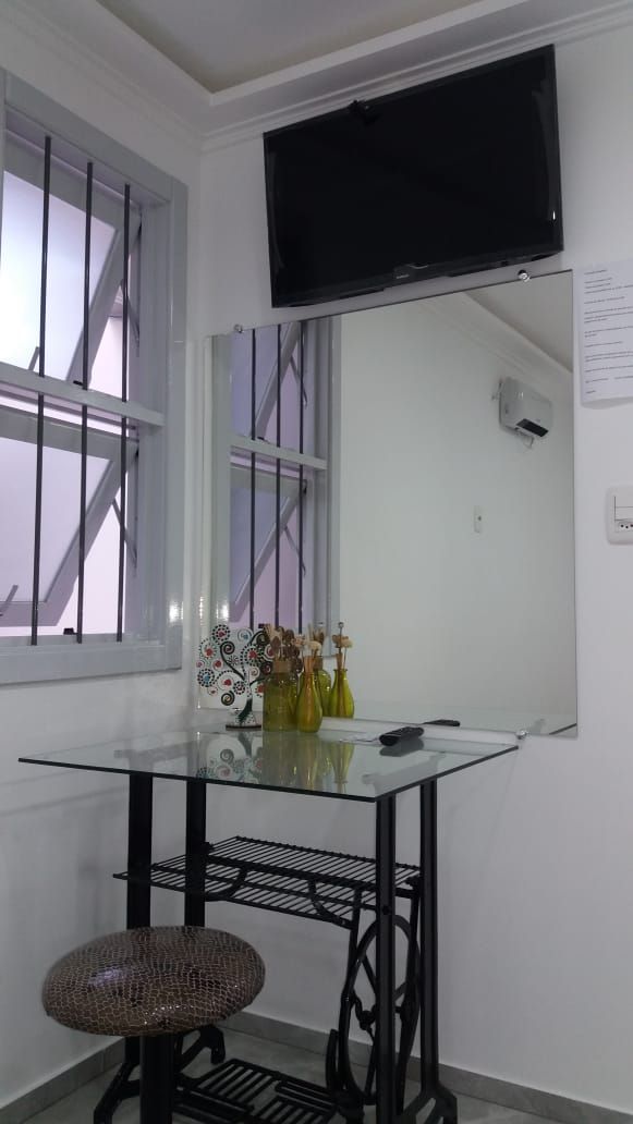 A small, modern room with a glass table, a wicker chair, and a mounted TV.