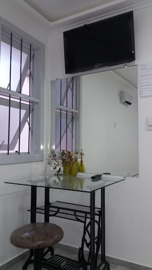 Ein kleiner, moderner Raum mit einem Glastisch, einem Korbstuhl und einem an der Wand montierten Fernseher.
