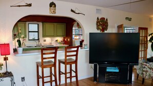 A kitchen with green cabinets, a dining area with two wooden chairs, a flat-screen TV, and a red lamp. - Beautiful Zen Temple Home on Canyon Lake! (Canyon Lake)