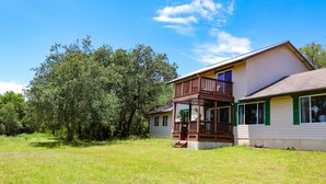 A two-story house with a balcony, surrounded by a grassy yard and trees. - Beautiful Zen Temple Home on Canyon Lake! (Canyon Lake)