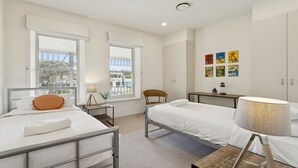 A modern bedroom with two beds, a chair, a small table, and a wall with colorful artwork. - Koonya Sur Mer Coastal Sorrento Escape (Sorrento)