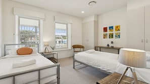 Ett modernt sovrum med två sängar, en stol, ett litet bord och en vägg prydd med färgstarka konstverk.