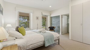 Ein Schlafzimmer mit einem Bett, einem Nachttisch, einer Lampe und Blick ins Freie durch ein Fenster.