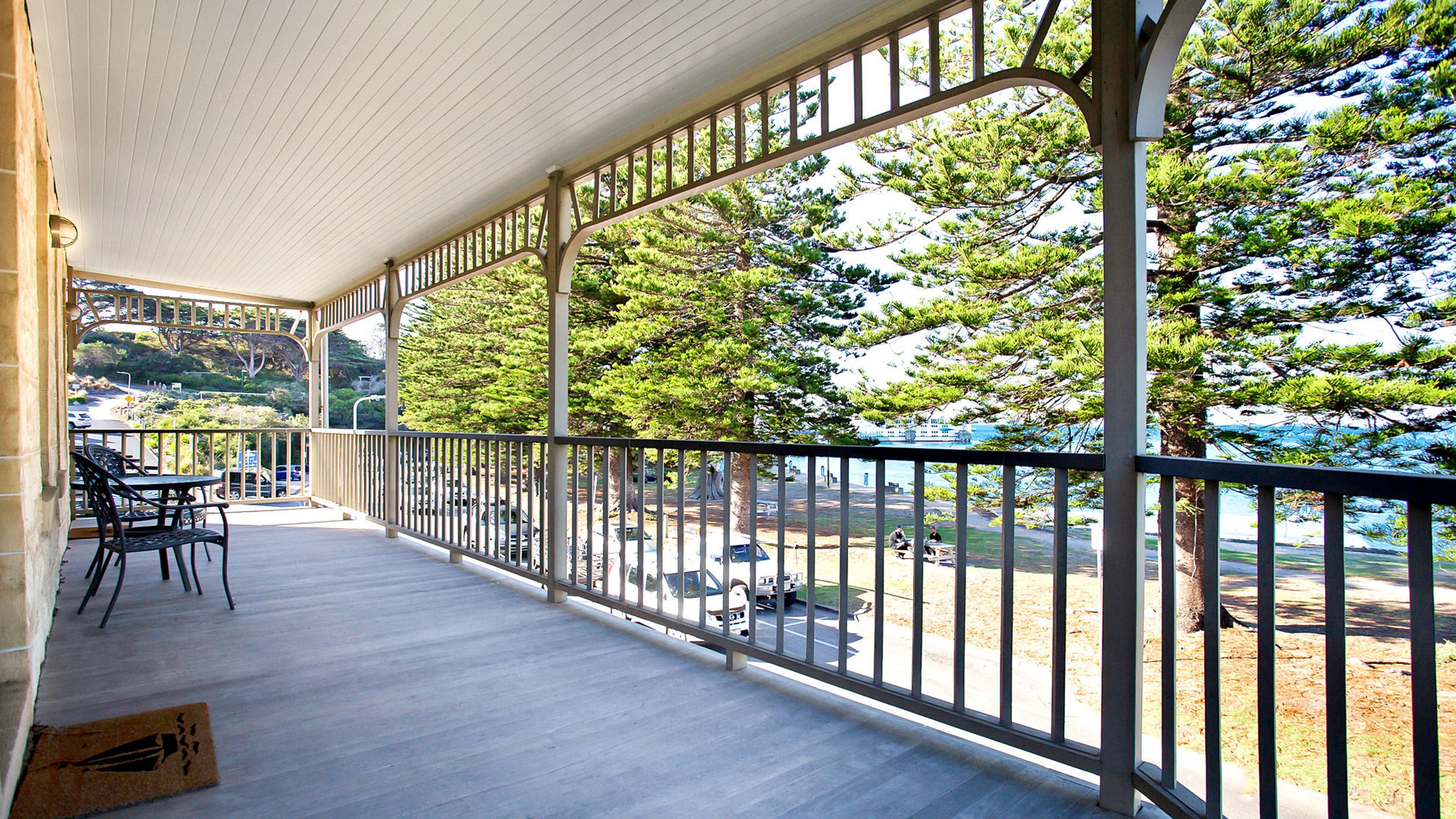A covered outdoor area with a railing, a table and chairs, and a view of trees and a road.