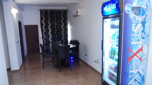 A room with a refrigerator stocked with beverages, a dining table with chairs, and a patterned curtain. - Kings Court Apartment (Abuja)