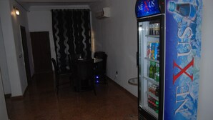 A room with a refrigerator stocked with beverages, a dining table with chairs, and a patterned curtain. - Kings Court Apartment (Abuja)