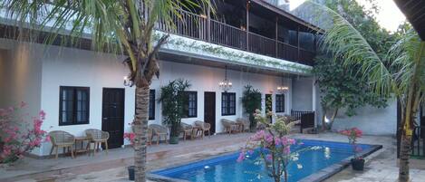 A courtyard with a swimming pool, outdoor seating, and a building with a balcony.