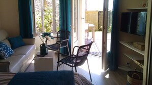 Une pièce comprenant un canapé, un fauteuil, un téléviseur et une porte-fenêtre coulissante donnant sur un espace extérieur.