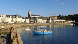 Une ville côtière dotée de bâtiments historiques, d’un clocher d’église imposant et de bateaux amarrés le long du quai.