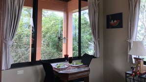 A dining area with a table set for two, a chair, a lamp, and a window with curtains.