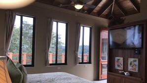 A bedroom with a bed, three windows, a ceiling fan, and a television on the wall.