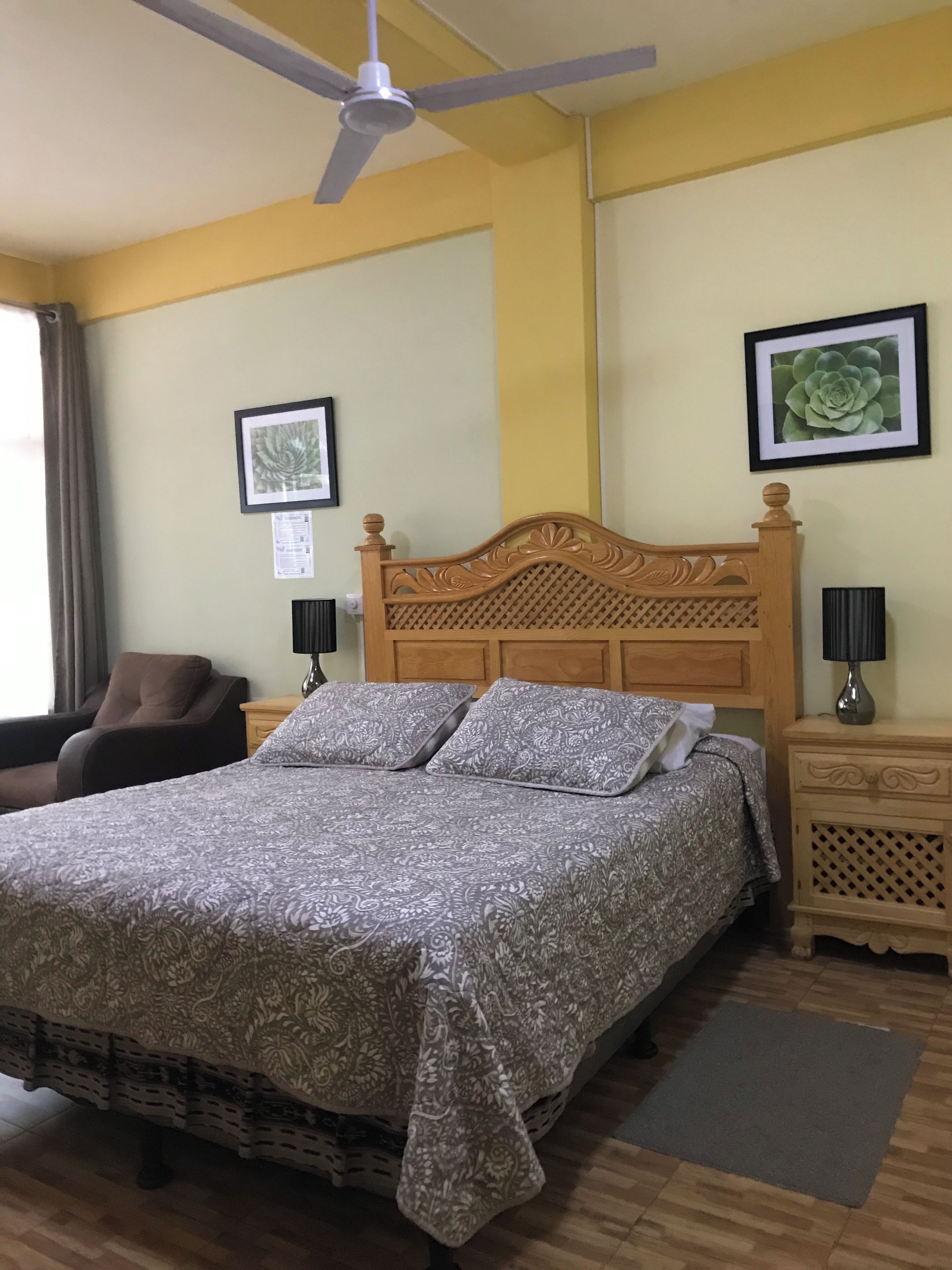 A hotel room with a bed, a chair, a nightstand, a lamp, and a ceiling fan.