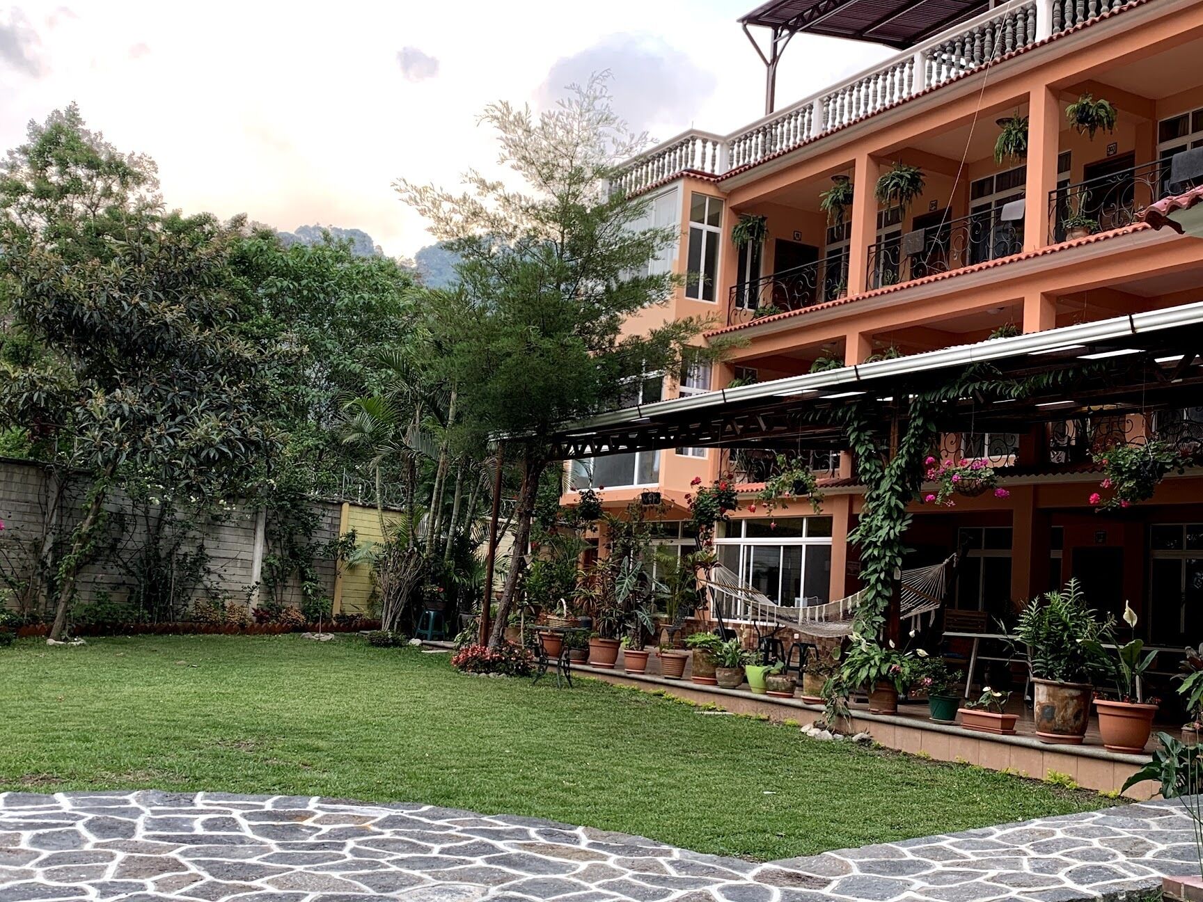 A multi-story building with balconies, potted plants, and a well-maintained lawn.