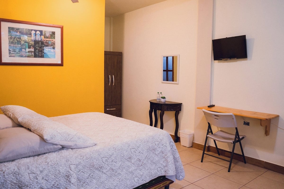 Un dormitorio con cama, escritorio, silla, televisor y armario.
