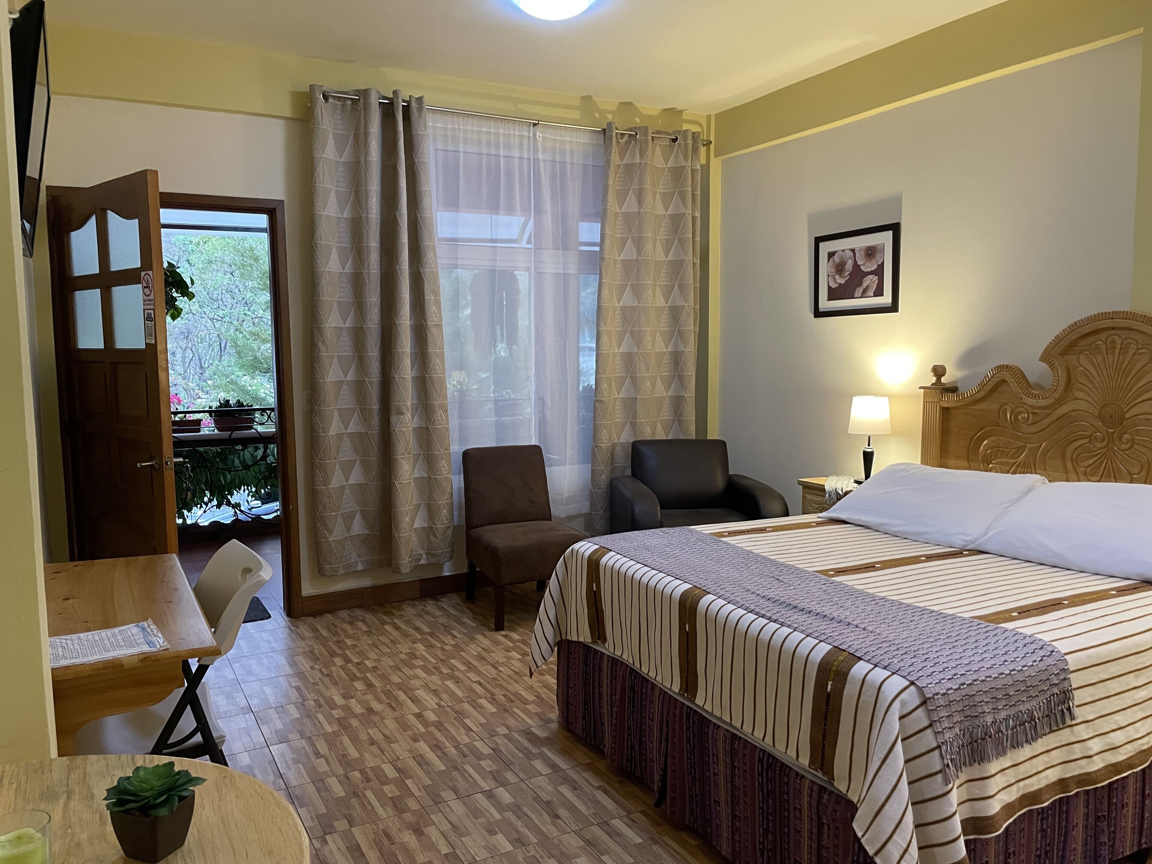 Una habitación de hotel con cama, una silla, un escritorio y un ventanal con cortinas.