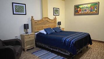 A bedroom with a wooden bed, two bedside tables, a nightstand, a blue and black striped rug, and two framed pictures on the walls.