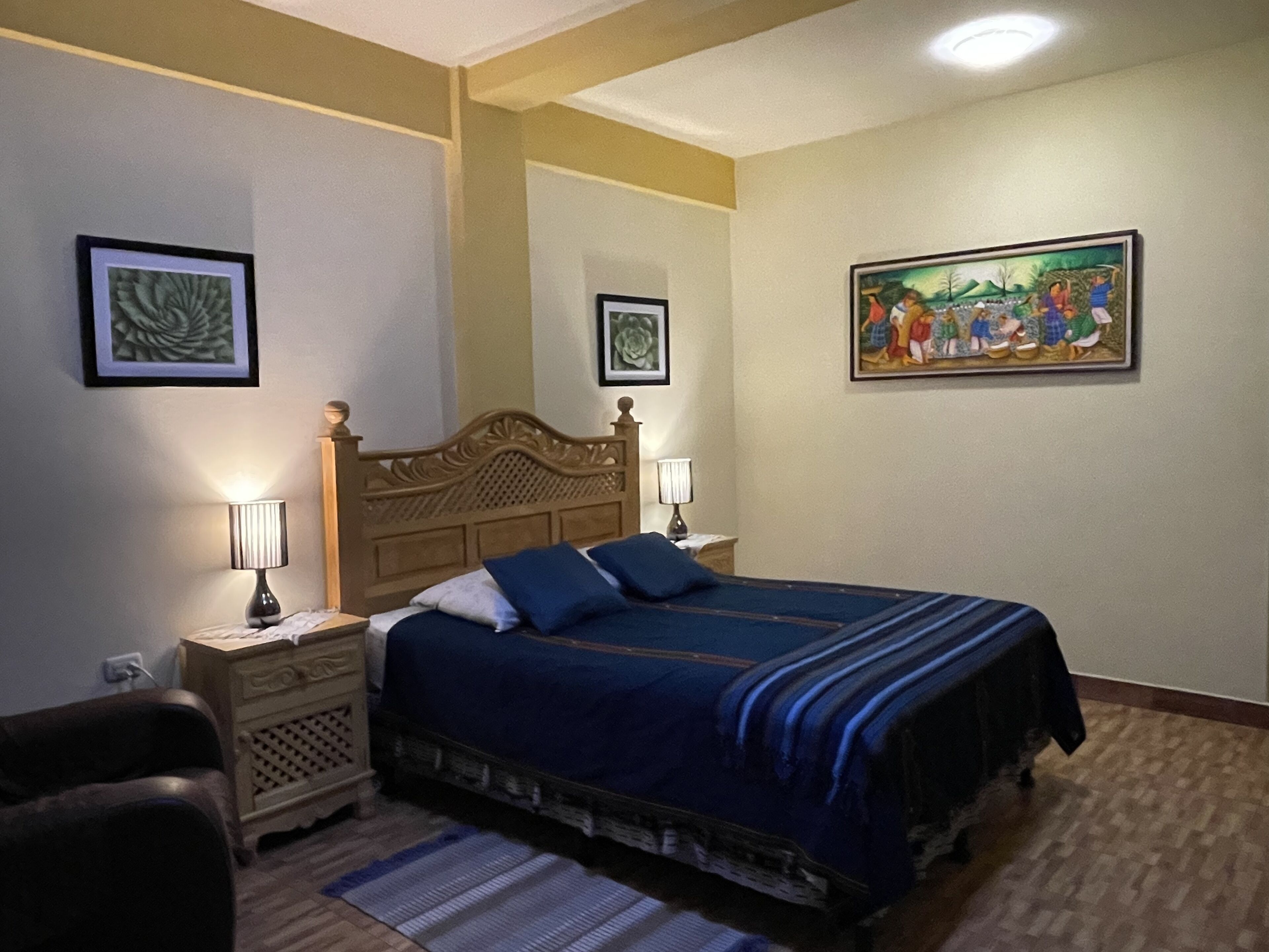 A bedroom with a large bed, two bedside tables with lamps, a wooden headboard, and two framed pictures on the walls.