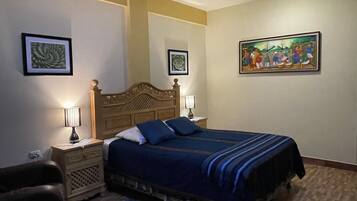 A bedroom with a large bed, two bedside tables with lamps, a wooden headboard, and two framed pictures on the walls.