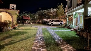 A well-lit courtyard with a stone pathway, a parked car, and a small red-roofed structure. - Jabel Tinamit Hotel & Villas (Panajachel)