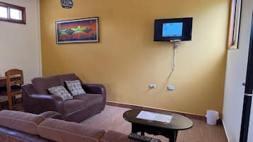 Ein Wohnzimmer mit einem braunen Ledersofa, einem kleinen Tisch mit Papieren, einem Wand-Fernseher und einem Bild an der Wand.