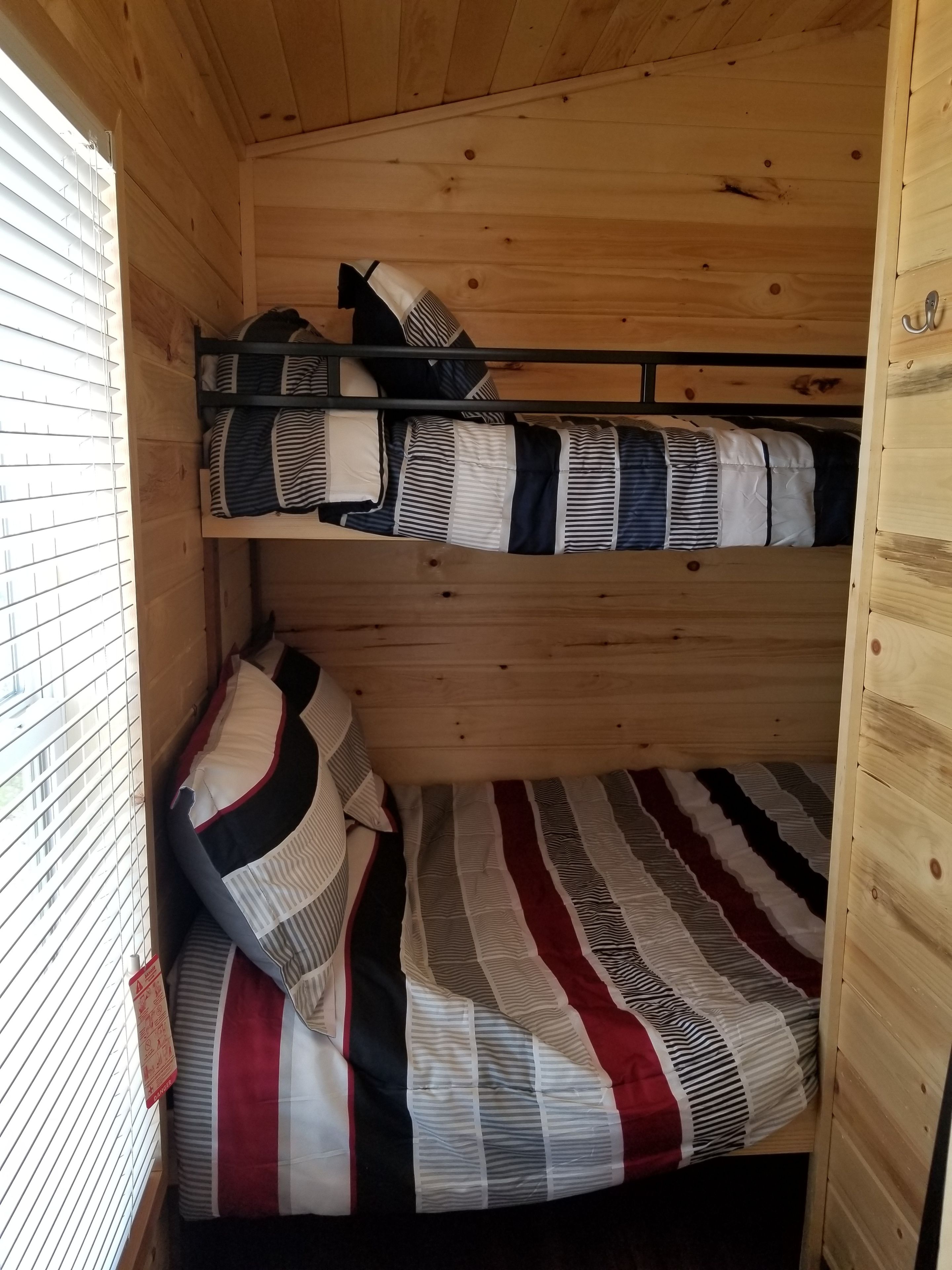 A bunk bed room with striped bedding and a window with blinds.